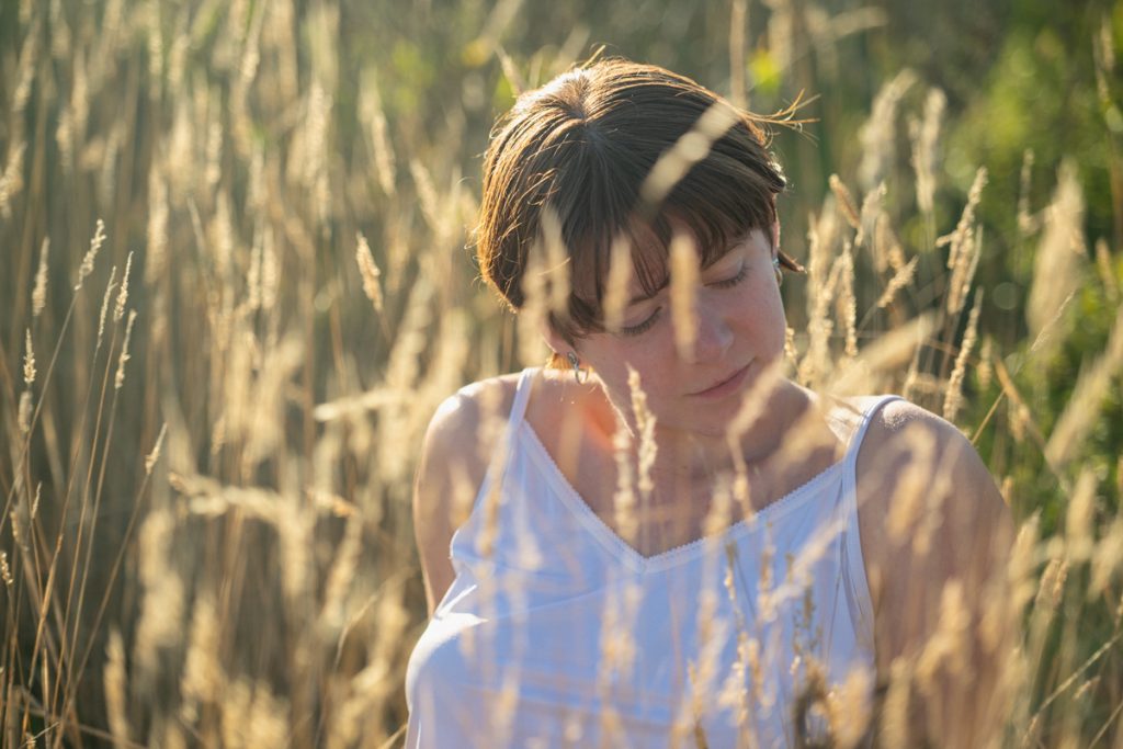 Woman in a white dress standing among tall golden grasses in warm sunlight