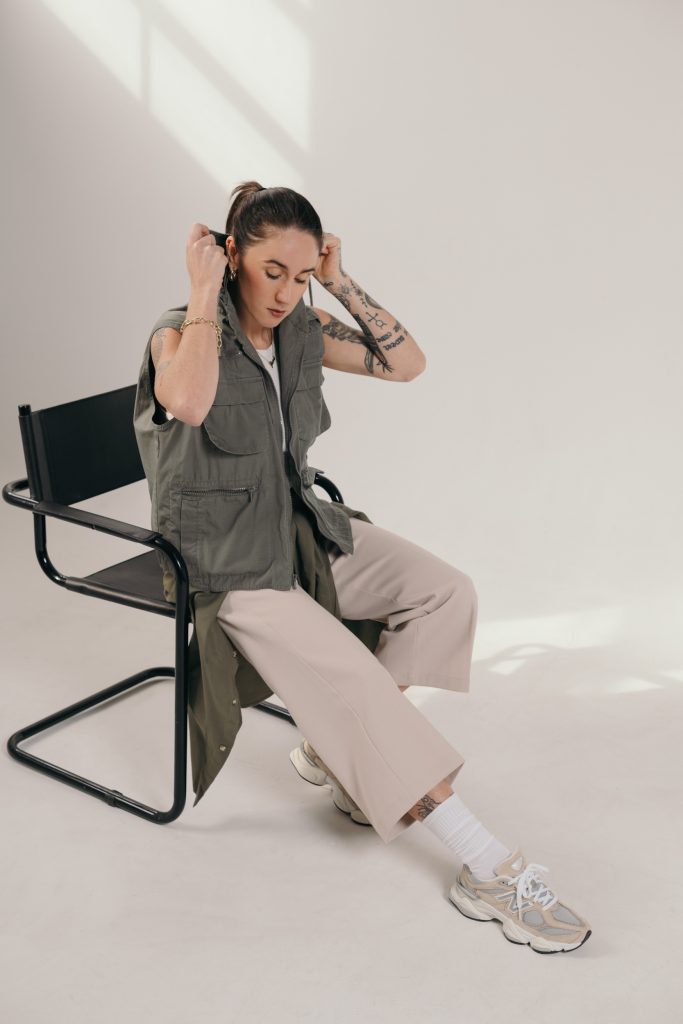 Fashion model seated in a black chair wearing neutral streetwear and sneakers